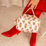 Trousse vanity N°50 Rose tenue par la poignée, escarpins et collants rouges