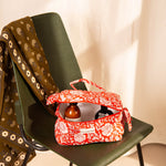 Trousse vanity Antioche Tomato ouverte avec des soins, sur une chaise vert foncé
