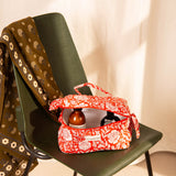 Trousse vanity Antioche Tomato ouverte avec des soins, sur une chaise vert foncé