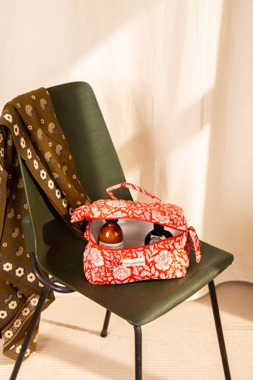 Trousse vanity Antioche Tomato ouverte avec des soins, sur une chaise vert foncé