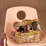 Trousse vanity Carthage Kaki ouverte, avec brosse et flacons, sur une chaise rose