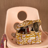 Trousse vanity Carthage Kaki ouverte, avec brosse et flacons, sur une chaise rose