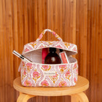 Trousse vanity Éphèse Rose ouverte avec flacon et maquillage, sur un tabouret