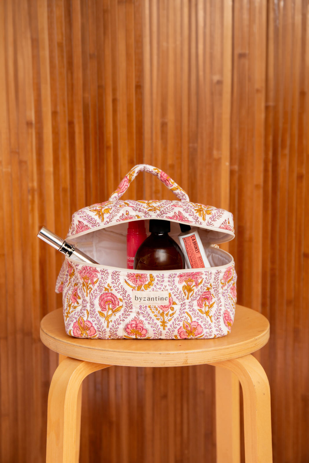 Trousse vanity Éphèse Rose ouverte avec flacon et maquillage, sur un tabouret