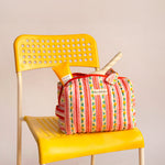 Trousse vanity Flora Rose à poignée posée sur une chaise jaune, avec des soins