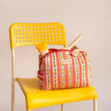 Trousse vanity Flora Rose à poignée posée sur une chaise jaune, avec des soins