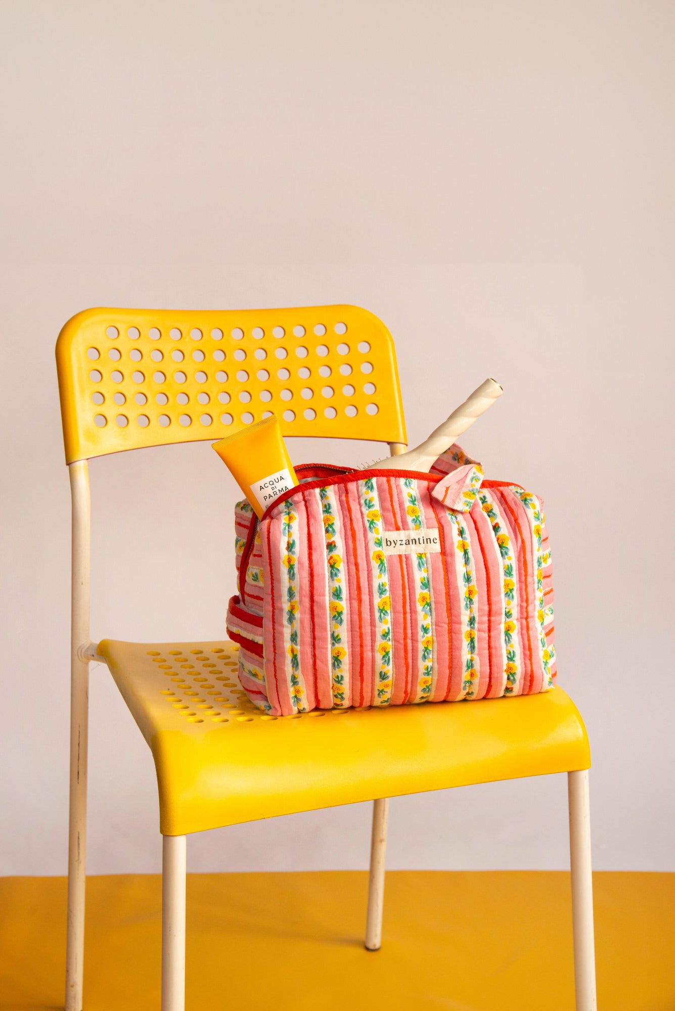 Trousse vanity Flora Rose à poignée posée sur une chaise jaune, avec des soins