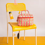 Trousse vanity Flora Rose de Byzantine sur une chaise jaune, avec une crème