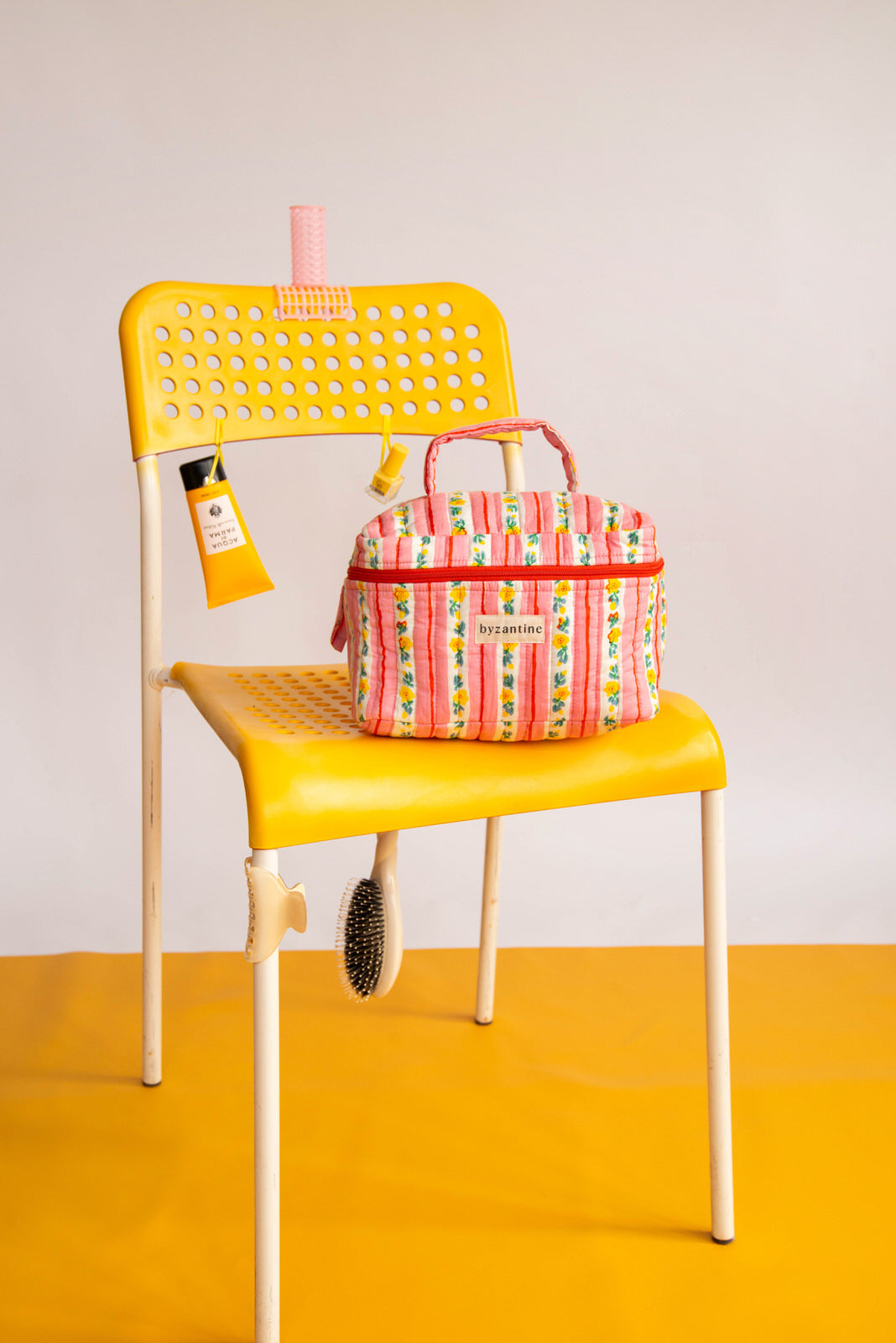 Trousse vanity Flora Rose de Byzantine sur une chaise jaune, avec une crème