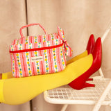 Trousse vanity Flora Rose posée sur des jambes en collants jaunes, escarpins rouges