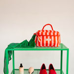 Trousse vanity Pacha Tomato à poignée sur une étagère verte, avec un foulard vert