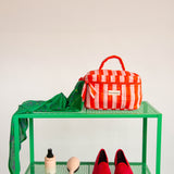 Trousse vanity Pacha Tomato à poignée sur une étagère verte, avec un foulard vert