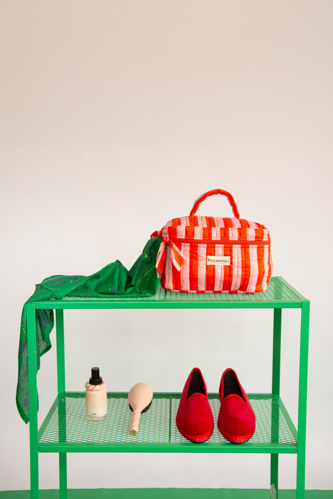 Trousse vanity Pacha Tomato à poignée sur une étagère verte, avec un foulard vert