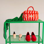 Trousse vanity Pacha Tomato à poignée, rayures rouge et rose, sur une étagère verte