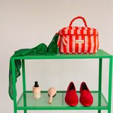 Trousse vanity Pacha Tomato à poignée, rayures rouge et rose, sur une étagère verte