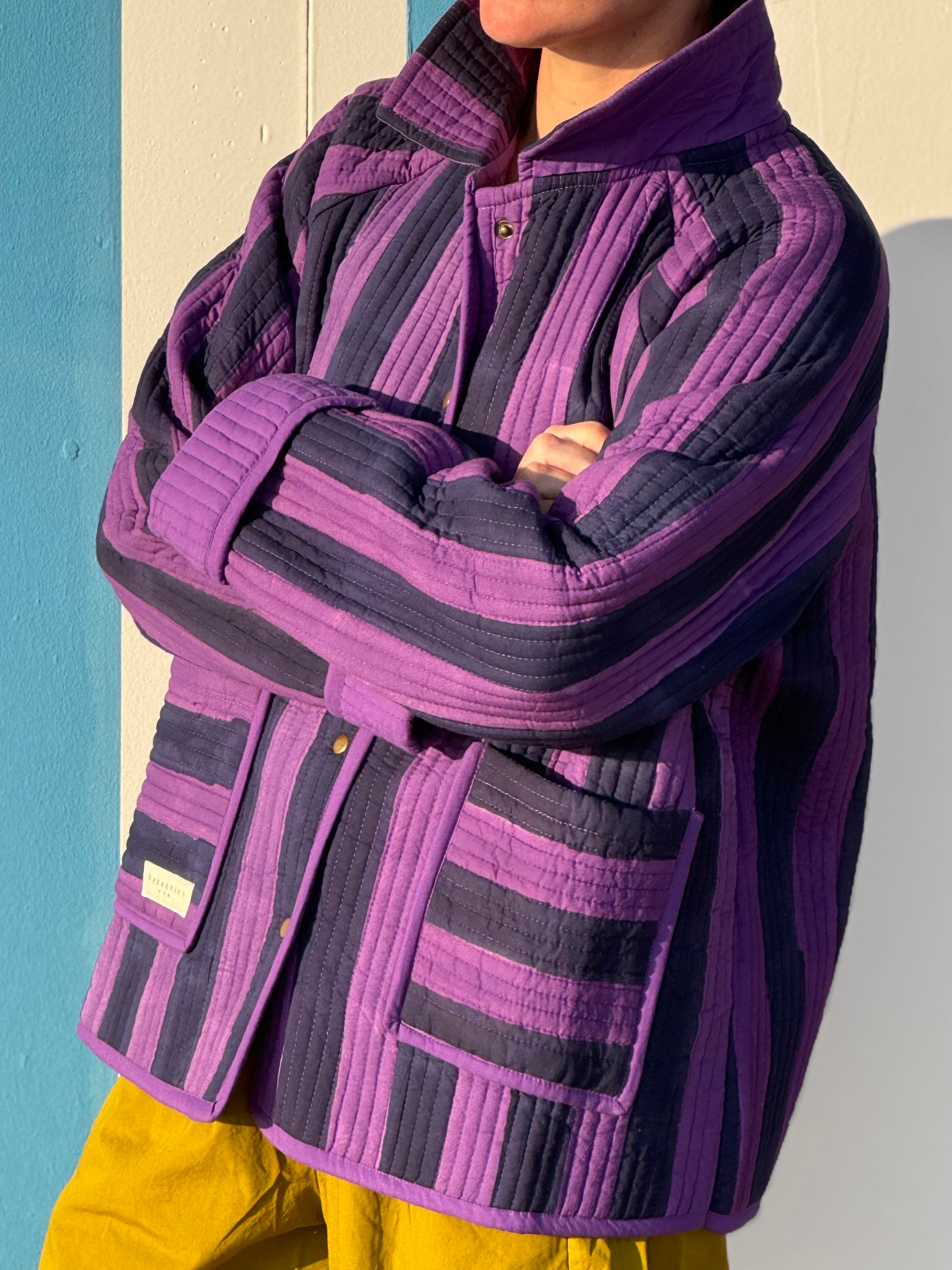 Veste matelassée Joseph portée bras croisés, larges rayures violet et bleu nuit, poches plaquées